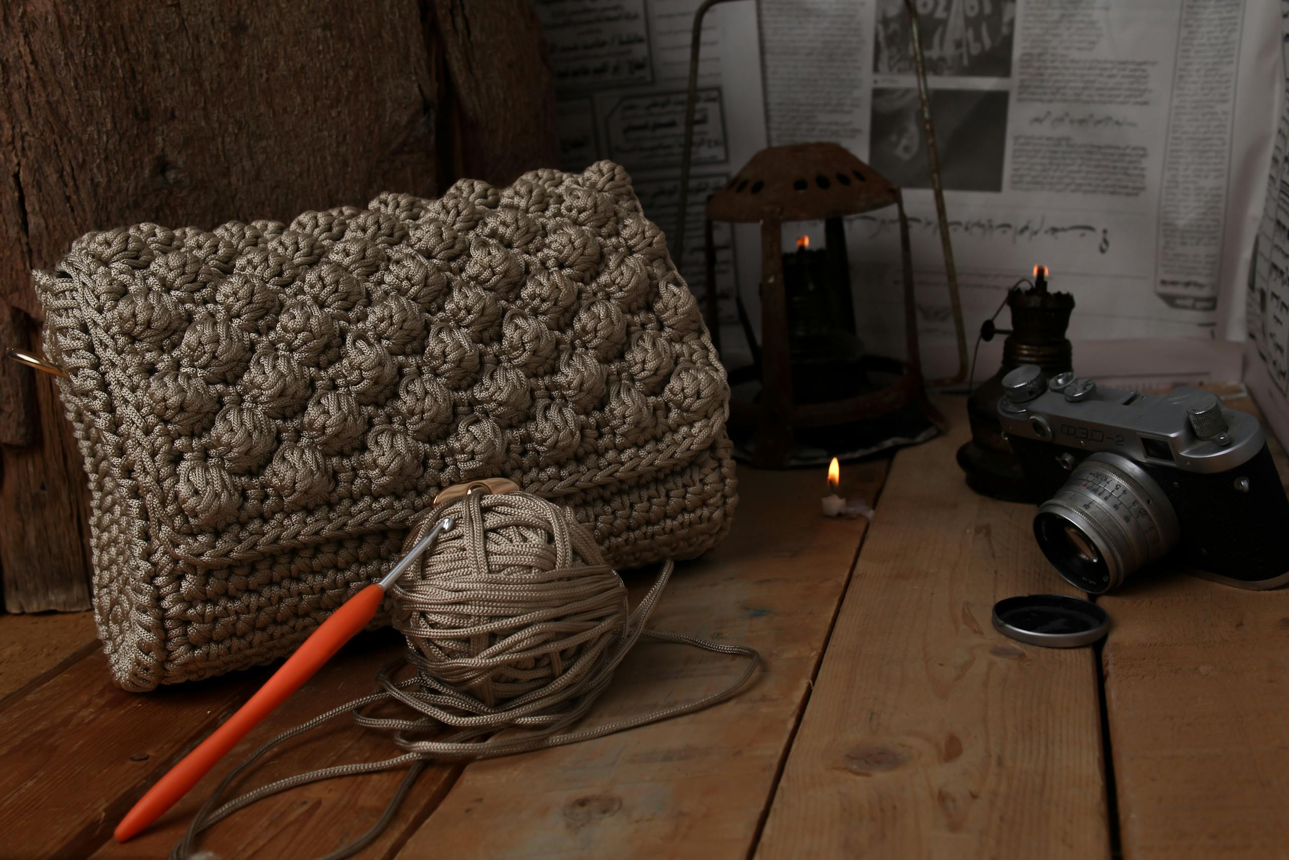 A rustic scene featuring a handcrafted crochet bag, vintage camera, and candle-lit ambiance.
